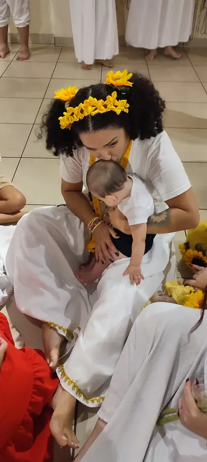 Mulher de coroa de flores amarelas beijando um bebê no colo.