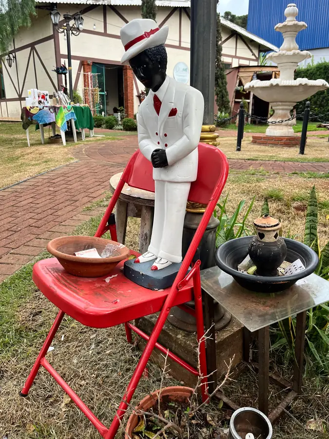 Estátua de caboclo ao ar livre, junto a uma cadeira vermelha.