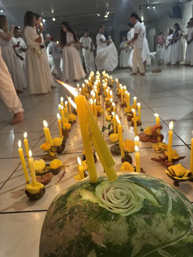 Fileira de velas acesas e flores ao redor de uma melancia decorada.